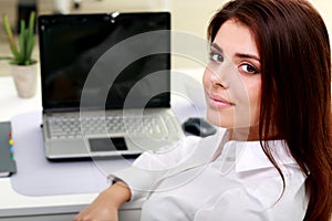 Happy young businesswoman sitting at the table on her workplace