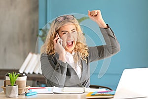 Happy young businesswoman talking on phone in office