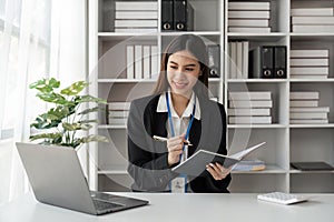 Happy young businesswoman working on laptop and taking notes in office