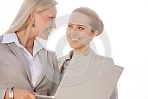 Happy young businesswomen with laptop looking at each other against sky