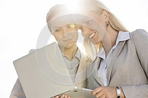Happy young businesswomen using laptop against sky