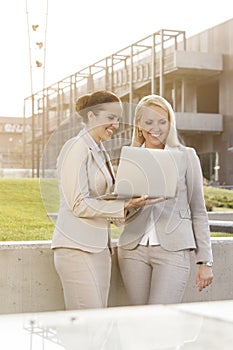 Happy young businesswomen using laptop together while standing against building