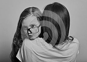 Happy young casual mother hugging and supporting her serious pupil sad kid in fashion glasses on purple background with empty copy