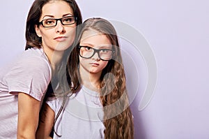 Happy young casual mother and serious sad kid in fashion glasses hugging on purple background with empty copy space