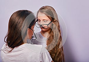 Happy young casual mother speaking and supporting her serious pupil sad kid in fashion glasses on purple background with empty