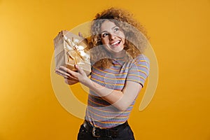 Happy young casual woman holding present box over yellow