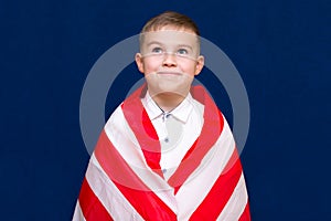 Happy young caucasian american boy kid child schoolboy wraps himself in a U.S. flag and look at camera