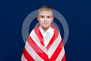 Happy young caucasian american boy kid child schoolboy wraps himself in a U.S. flag and look at camera