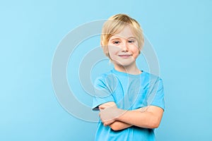 Happy young caucasian boy in casual outfit smiling with arms crossed isolated over pastel blue background.