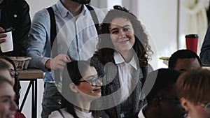 Happy young Caucasian business woman in formal clothes listening to speaker at modern multiethnic office meeting seminar