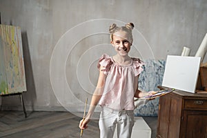 Happy young Caucasian child holding palette of colors in hand