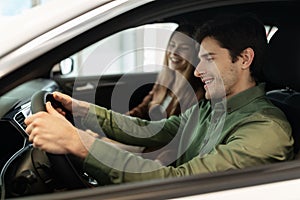 Happy young Caucasian couple driving their new car, sitting inside luxury auto, copy space