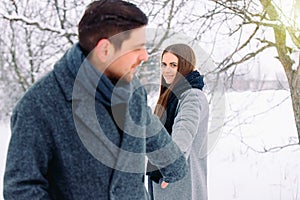 Happy young caucasian couple holding hands and looking at each other, smiling cute, while walking in winter forest