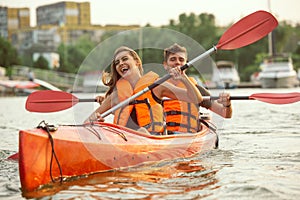 Happy couple kayaking on river with sunset on the background