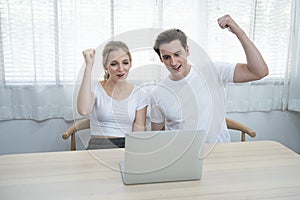 Happy young caucasian couple with laptop hand rise up with happy and fun moment spending time together at home