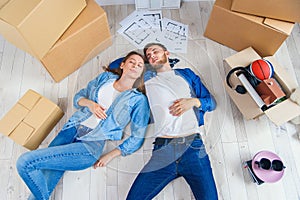 Happy young caucasian couple lying down on the wooden floor while having a break while moving to new house. Top view.