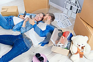 Happy young caucasian couple lying down on the wooden floor and messaging at smart phones during having break while