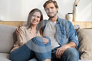 Happy young Caucasian couple relax on cozy sofa at home hugging look in distance dreaming together