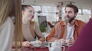 Happy young Caucasian couple talking with friends in restaurant. Cheerful man and woman resting in cafe with fellows