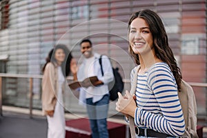 Happy young caucasian girl smiling looking at camera standing on blurred background of classmates.