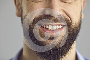 Closeup studio shot of lower part of face of happy smiling young man with brown beard