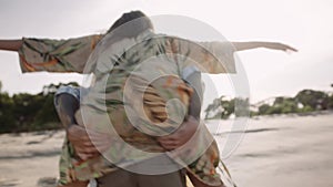 Happy young caucasian man carrying girlfriend on back while spinning at the beach