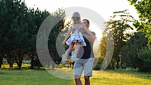Happy young Caucasian man playing with little pretty daughter on nature. Joyful loving dad spinning his cute child girl