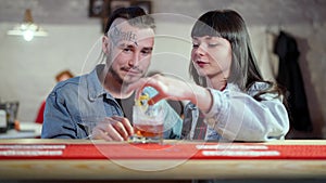 Happy young Caucasian modern couple sitting at bar counter smiling and talking. Millennial man with tattoo on face and
