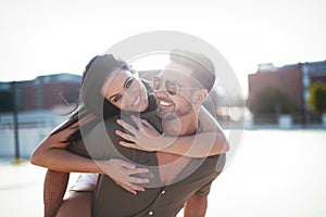 Happy young caucasian urban couple doing piggyback and smiling at outdoors