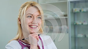 Happy young Caucasian woman blonde doctor in white medical coat and stethoscope looking at camera. Close-up face