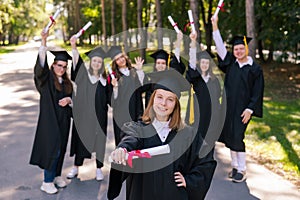 Happy young caucasian woman celebrating graduation with classmates. A group of graduate students outdoors.