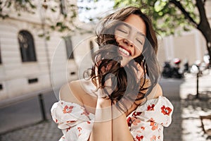 Happy young caucasian woman with closed eyes smiles teeth resting on street.