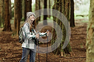 Happy young caucasian woman in jacket with trekking sticks walk enjoy trip alone in forest