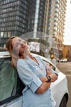 Happy young caucasian woman leaning on car on street