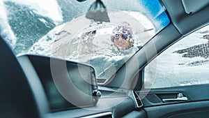 Happy young caucasian woman in pink jacked cleaning irst snow from her car