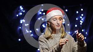 Happy young caucasian woman in Santa hat waving hand and holding sparkler.