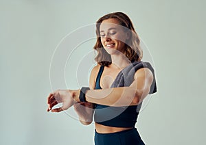 Happy young caucasian woman in sports clothing looking down while using fitness tracker in studio
