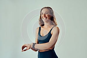 Happy young caucasian woman in sportswear looking away while using fitness tracker in studio