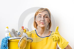Happy young caucasian woman in a uniform wearing yellow rubber gloves and holding bucket full of cleaning supplies. Cleaning