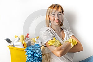 Happy young caucasian woman in yellow rubber gloves holding bucket full of cleaning supplies. Cleaning company service