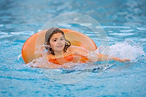 Happy young child enjoying summer vacation outdoors in water in the swimming pool. Cute little kid in swimming suit swim