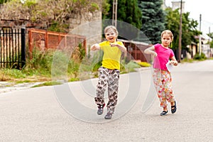 Happy young children on the town street, two joyful cheerful little school age girls jumping, walking on the street together