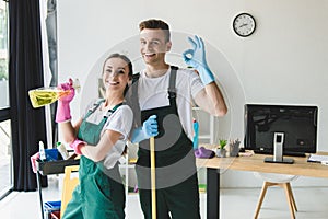 happy young cleaning company workers holding cleaning equipment and showing