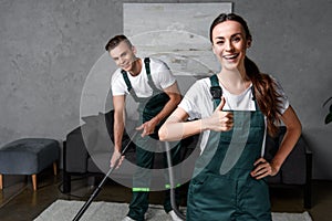 happy young cleaning company workers using vacuum cleaner and showing