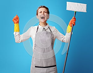 Happy young cleaning woman in apron on blue with mop rejoicing