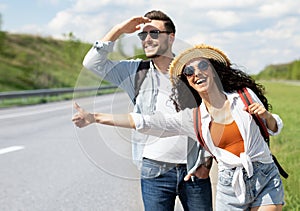 Happy young coupe flagging down car, needing ride, hitchhiking on roadside outdoors