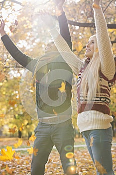 Happy young couple with arms raised enjoying falling autumn leaves in park