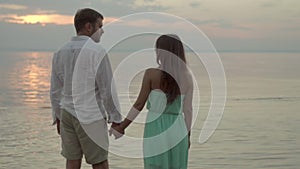 Happy young couple on the beach on sunset they hold hands and look to each other