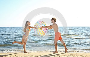 Happy young couple in beachwear playing with inflatable ball