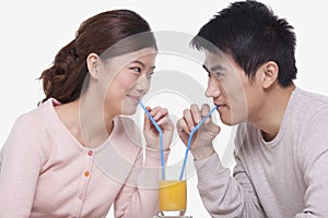 Happy young couple bonding and sharing a glass of orange juice, studio shot